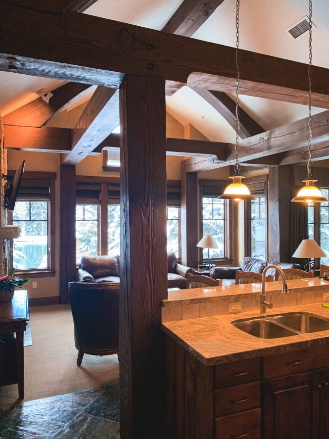 indoor of ski villa overlooking kitchen and living space with big wood beams and cozy cabin feel