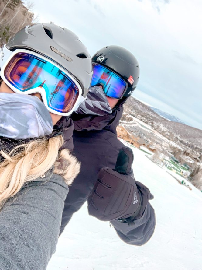 husband and wife giving thumbs up in picture together on top of snowy mountain at deer valley ski resort in utah