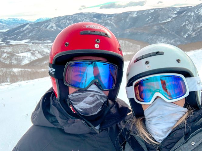 husband and wife in goggles and helmets in the winter snow in utah to go snowmobiling