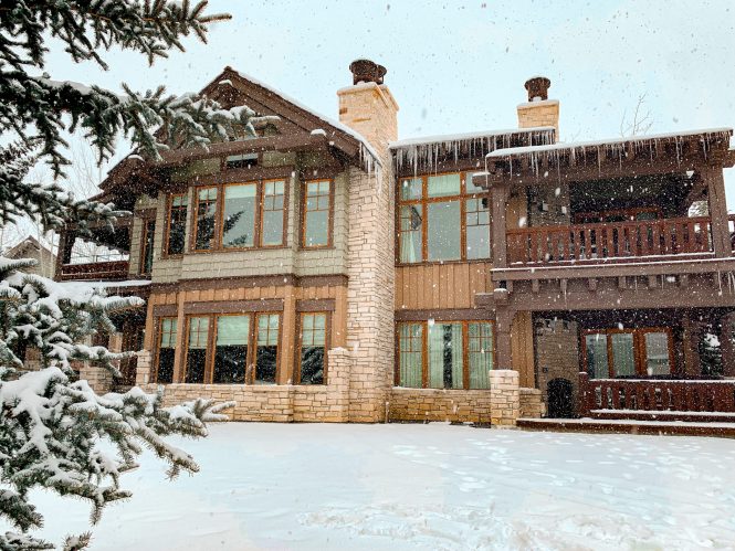 back of a hotel villa in the snow and pine trees with large scenic windows overlooking a lake