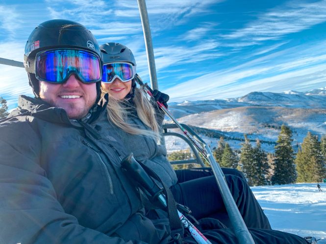 husband and wife on ski lift with mountain and snow in the background